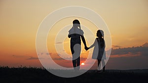 Happy family two sisters walks at sunset in the park silhouette. two daughters hold hands outdoors. kid dream concept