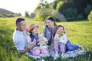 Happy family with two small daughters sitting outdoors in spring nature, having picnic.
