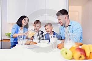 Happy family with two sons eating healthy morning breakfast with cornflakes and milk on cozy kitchen at dining table.