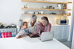 Happy family using graphic tablet while looking at laptop in kitchen