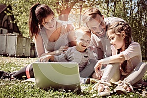 Happy family using laptop, sitting on the green grass.