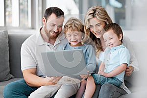 A happy family using a laptop on the sofa with children at home. Smiling man and woman relaxing online with their sons