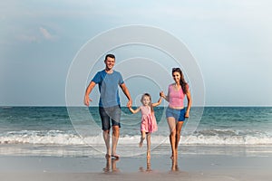Happy family on vacation. Mom, Dad and a little daughter are walking along the seashore. Traveling family
