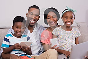 Happy family with various technologies sitting on sofa at home