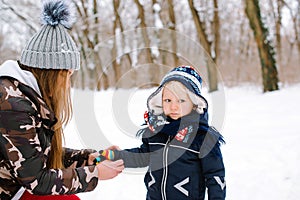 Happy family during walk at snowy forest. Mother helps her little son put on a warm gloves. Happy winter holidays. Snowy winter