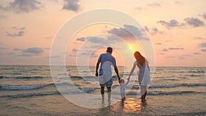 Happy family walking along the sea coast at sunset.