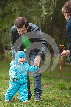 Happy family walking in autumn park: mother, father and his little son - learn to stroll independently