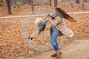 Happy family walking in autumn park. Young mother playing with son in fallen leaves. Mom spinning her toddler son. Family enjoy
