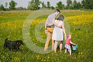 Happy family walking with black labrador dog in summer field
