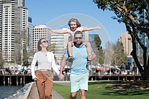 Happy family walking the city street, casual lifestyle. Portrait of mother and father giving son piggyback ride on his