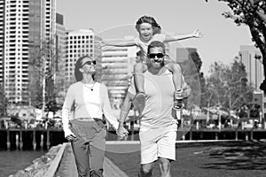 Happy family walking the city street, casual lifestyle. Portrait of mother and father giving son piggyback ride on his