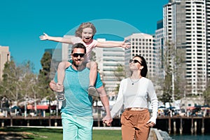Happy family walking the city street, casual lifestyle. Portrait of mother and father giving son piggyback ride on his