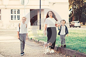 Happy family walking with dog in city street. Stylish mother and kids having fun with their dog outdoors