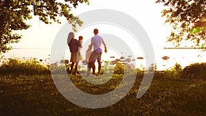 Happy family walking near the sea. Field and trees in countryside. Warm colors of sunset or sunrise. Loving parents and