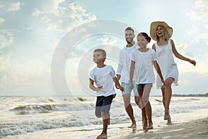 Happy family walking on sandy beach near sea at sunset