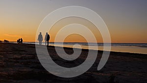 Happy family walking on sea coast. Silhouettes sunset.