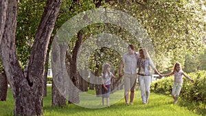 Happy family walking in summer Park near the blossoming Apple trees. father, mother and two daughters spend time