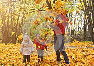 happy family walking in sunny park and throws orange maple leaves. mother with kids enjoying autumn weather outdoors