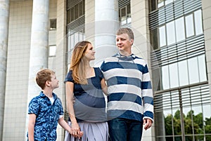 Happy family walking together. Pregnant mother, father and son spend time on city street
