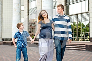 Happy family walking together. Pregnant mother, father and son spend time on city street