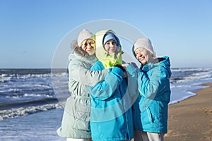 A happy family walks along the sandy seashore in winter. Laughing mother, grandmother and adult daughter hugging. Love and