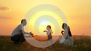 Happy family walks in park at sunset. Mom, dad and baby. Little daughter goes from mom to dad, hugs and kisses her