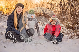 Happy family in warm clothing. Smiling mother and son making a snowman outdoor. The concept of winter activities