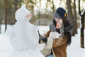 Happy family in warm clothing. Smiling mother and son making a snowman outdoor. The concept of winter activities