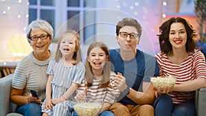 Happy family watching TV with popcorn at home.