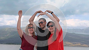 Happy family waving to camera and create a heart gesture with your hands against beautiful Mountain View. Tourists