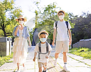 Happy family wearing the medical mask and walking in the park. Family vacations during coronavirus covid-19 pandemic