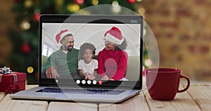 Happy family wearing santa hats on laptop video call, with christmas decorations and tree