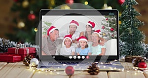 Happy family wearing snata hats on video call on laptop, with christmas decorations and tree