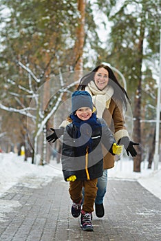 Happy family in winter clothing. Smiling son runs away from his mother outdoor