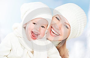 Happy family on a winter walk. Mother and baby daughter in the white hats
