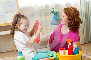 Happy family - woman and her cute little daughter are having fun, using a sprayer and a rag while cleaning their house