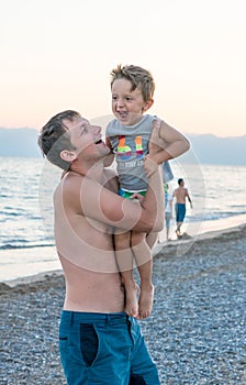 Happy family. Young beautiful father and his smiling son baby boy having fun on the beach of the sea, ocean. Positive human emotio