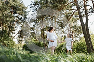 Happy family: a young beautiful pregnant woman with her little cute daughter on a sunny summer day. Parents and kids