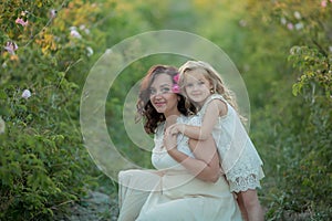 Happy family: a young beautiful pregnant woman with her little cute daughter walking in the wheat orange field on a