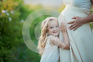 Happy family: a young beautiful pregnant woman with her little cute daughter walking in the wheat orange field on a