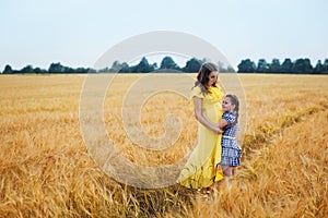 Happy family: a young beautiful pregnant woman with her little cute daughter walking in the wheat orange field on a sunny summer