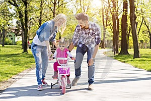 Happy family with young caucasian parents teaching their daughter how to ride a bike