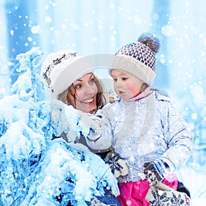 Happy family with young mother and child daughter on a winter walk outdoors. Kid toddler girl and beautiful woman having