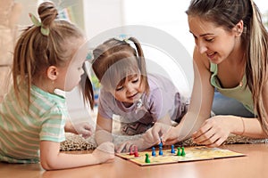 Happy family. Young mother playing ludo boardgame with her daughters while spending time together at home.