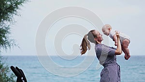 Happy family. Young mother throws up baby in the sky, on sunny day. Portrait mom and little son on the beach. Positive