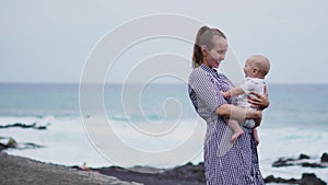 Happy family. Young mother throws up baby in the sky, on sunny day. Portrait mom and little son on the beach. Positive