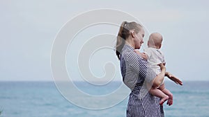Happy family. Young mother throws up baby in the sky, on sunny day. Portrait mom and little son on the beach. Positive