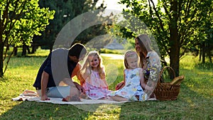 Happy family. Young parents spending time on nature with children sitting on a blanket. Handsome dad and beautiful mom