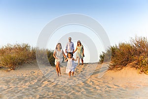 Happy family young parents two kids walking on sandy beach on sunny day during summer vacation