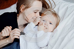 Happy family, young woman mother kisses baby in bed